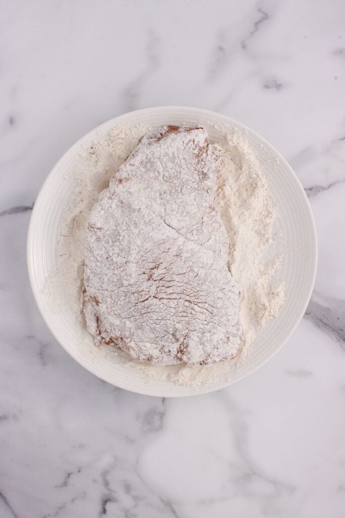 Round steak coated in flour on a dinner plate.