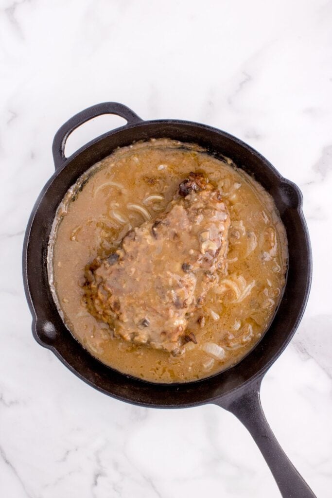 Cast iron pan with completed round steak and gravy.