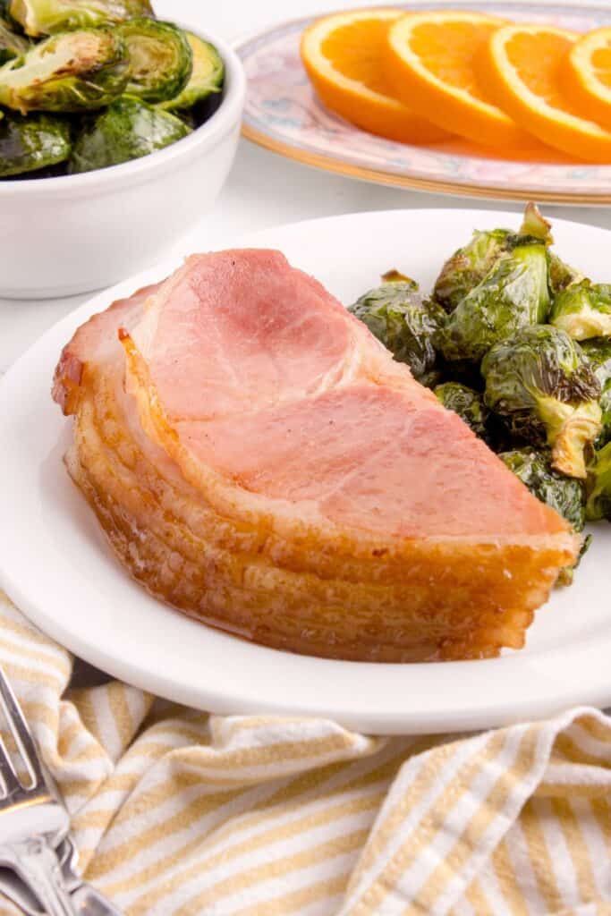 Several half slices of spiral ham on a dinner plate with brussel sprouts.