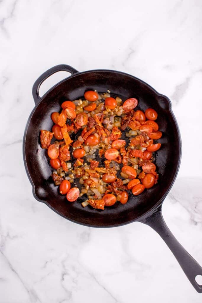 Sliced cherry tomatoes, onion, garlic, and sun dried tomatoes in a cast iron skillet