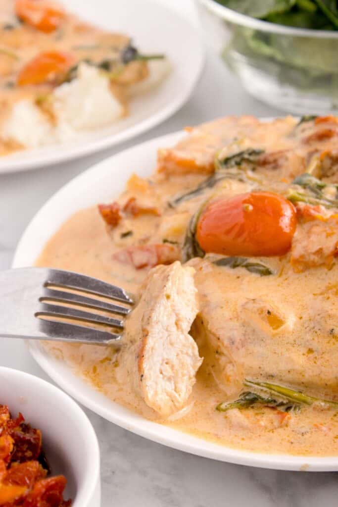 Completed chicken recipe on a white dinner plate. Fork is removing a bite from the plate to show the cooked interior of the chicken.