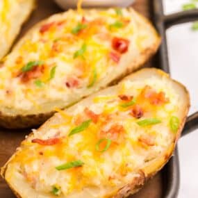 Completed twice baked potatoes in a baking sheet. Small bowl of crumbled bacon in the background.