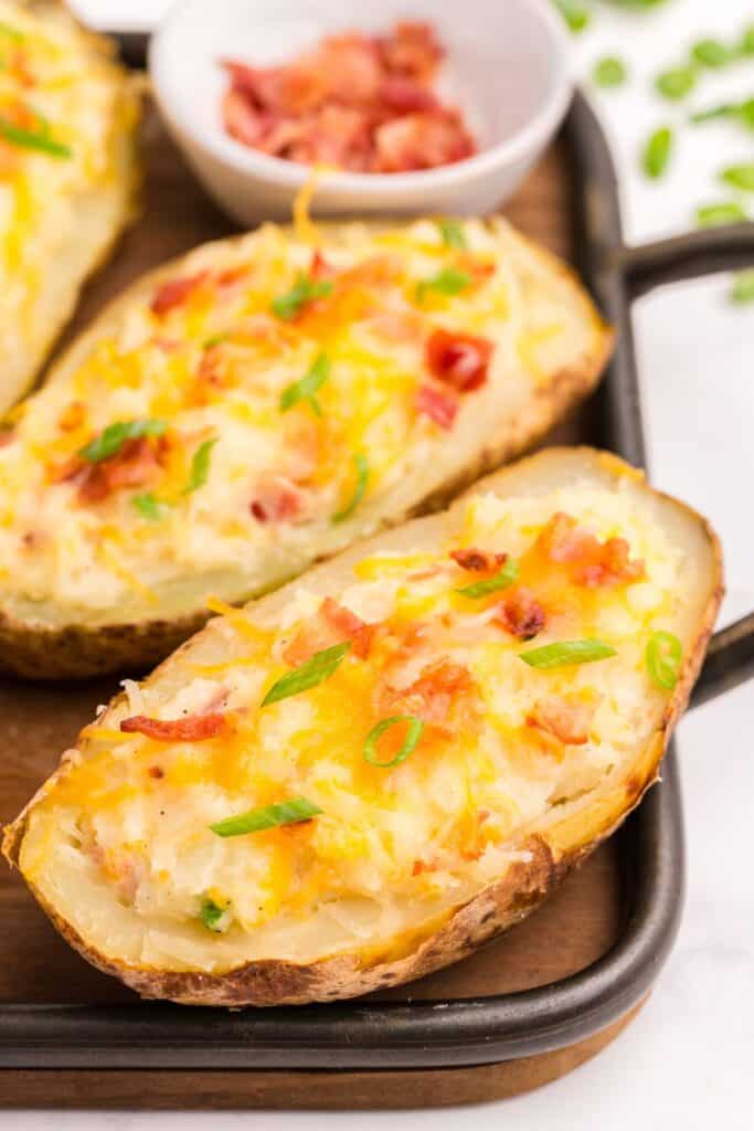 Completed twice baked potatoes in a baking sheet. Small bowl of crumbled bacon in the background.