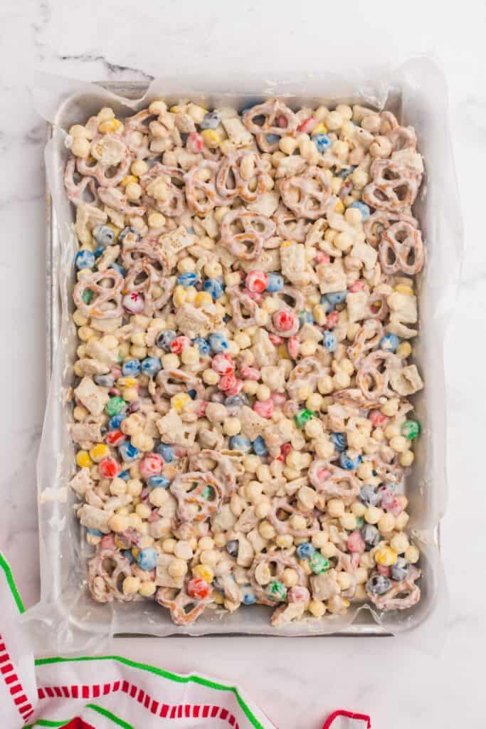 White trash candy (white chocolate chex mix candy) spread out on a baking sheet with parchment paper.