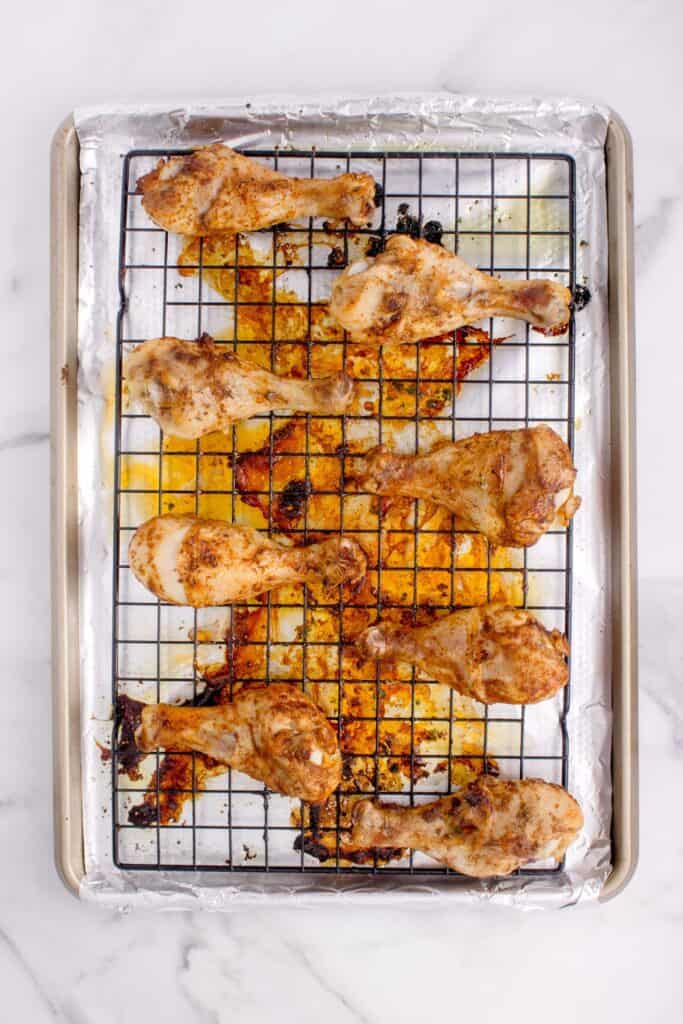 Overhead view of chicken legs after baking on a cooling rack, over an aluminum foil lined baking sheet.