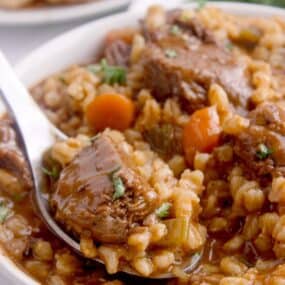 Close up image of a white soup bowl with beef and barley soup.