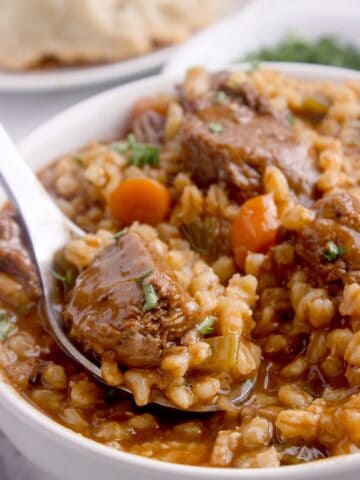 Close up image of a white soup bowl with beef and barley soup.