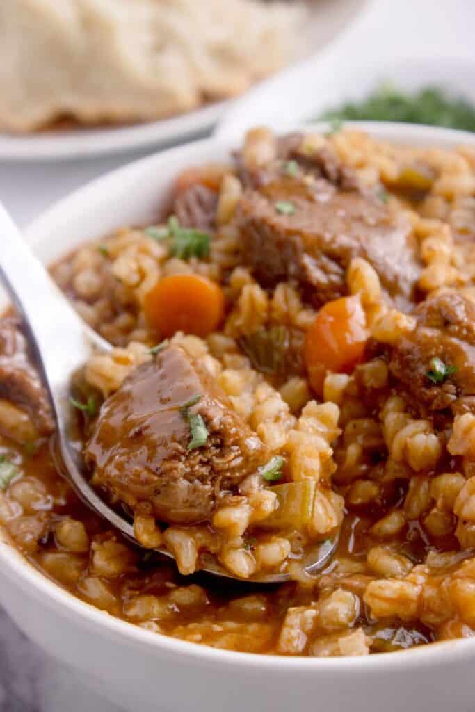 Close up image of a white soup bowl with beef and barley soup.