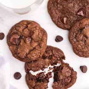 Overhead view of several cookies and a glass of milk. One cookie is broken up to show the gooey interior.