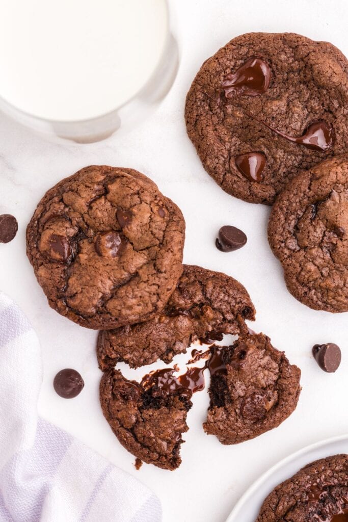 Overhead view of several cookies and a glass of milk. One cookie is broken up to show the gooey interior.