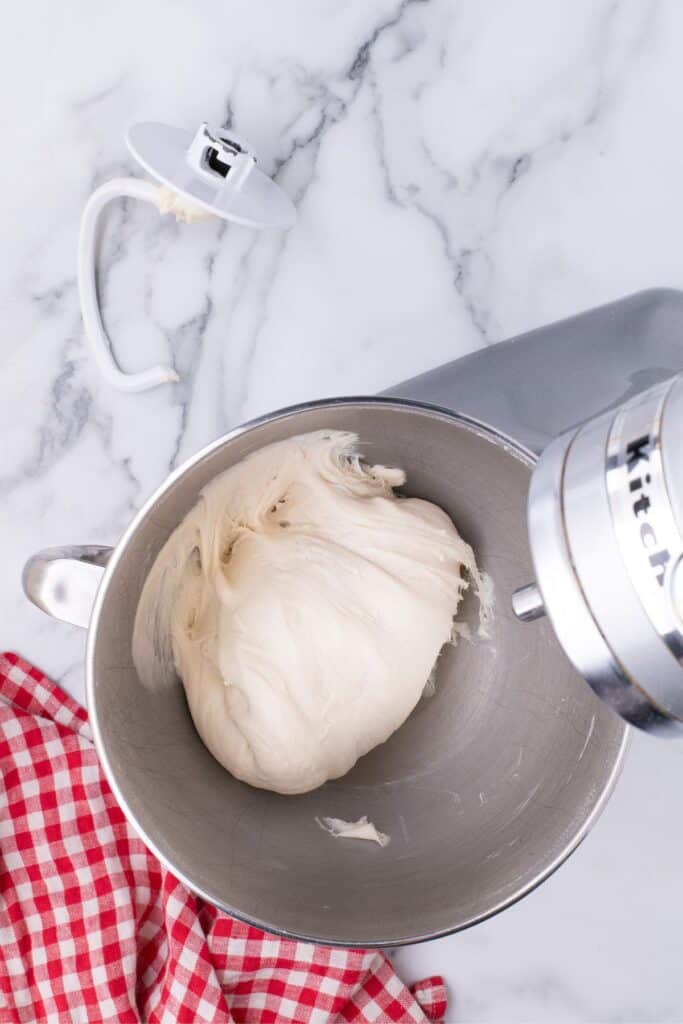 Kitchen Aid mixer with pizza dough in the bowl. Bread dough hook sitting just above to mixer.