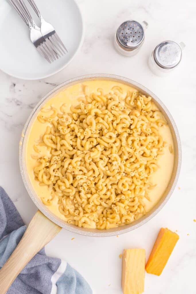 Large skillet with cheese sauce in it. Cooked pasta elbows have been added in the middle of the skillet.