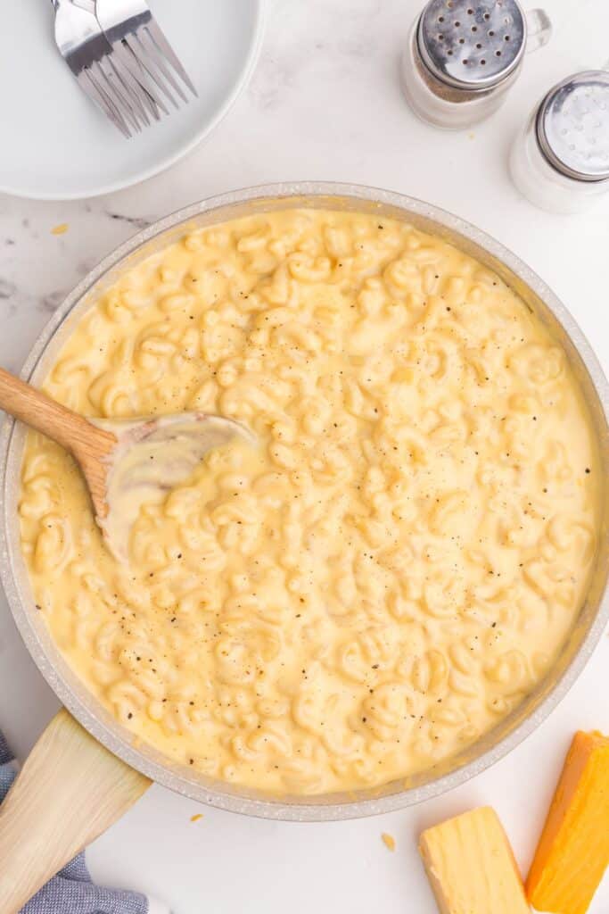 Overhead image of gouda mac and cheese in a large skillet with a wooden spoon.