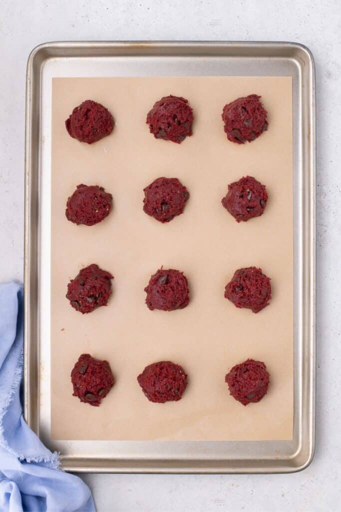 Unbaked red velvet cookies on parchment lined baking sheet.