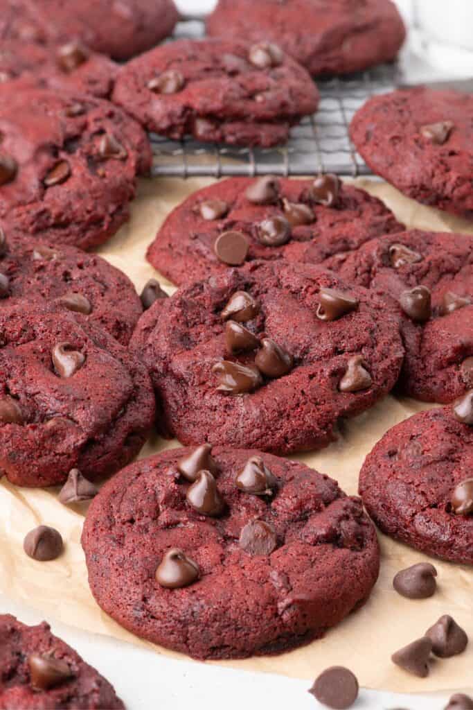 Side image of a pile of red velvet cookies sitting on a cooling rack and on parchment paper.