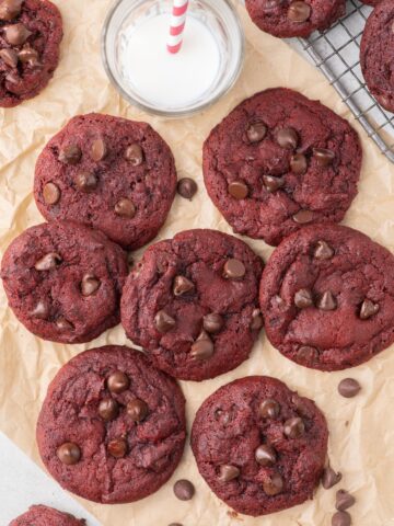 Pile of red velvet cookies on a strip of parchment paper with a glass of milk above.