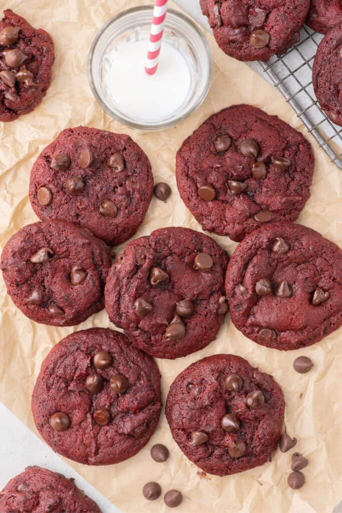 Pile of red velvet cookies on a strip of parchment paper with a glass of milk above.