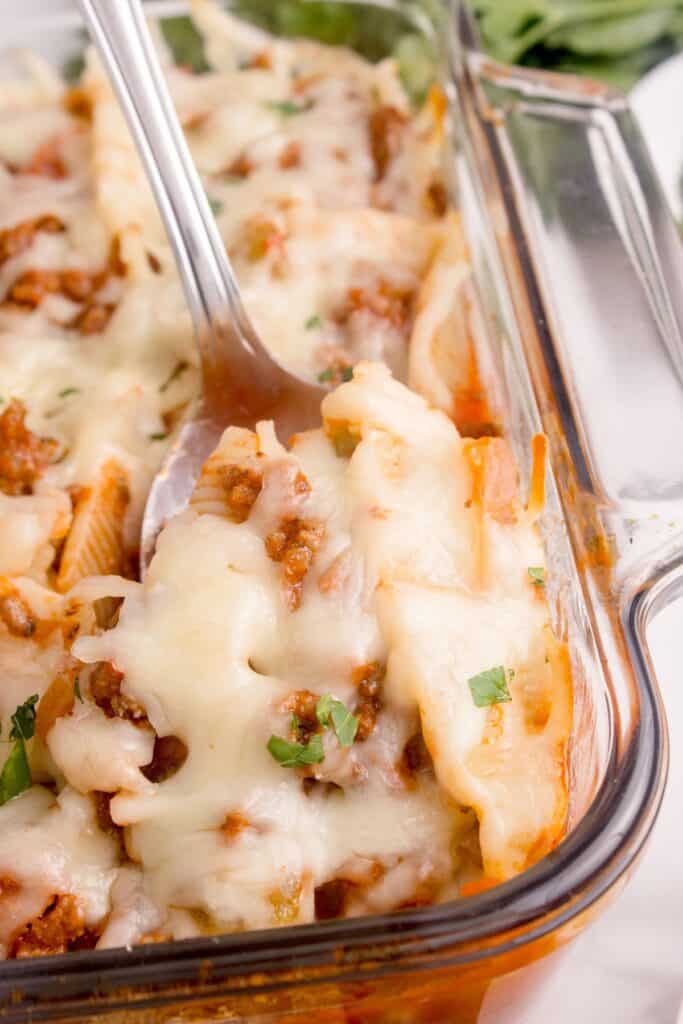 Close up of beef stuffed shells in a casserole dish with a serving spoon.