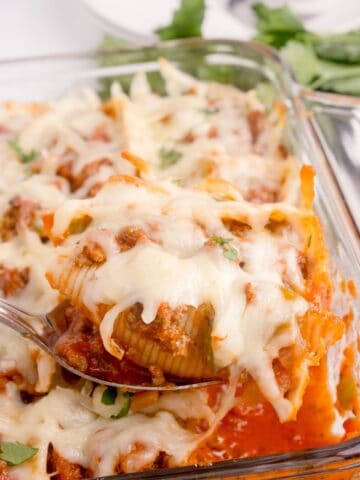 Casserole dish with beef shells. A serving spoon is lifting up a portion of the recipe.