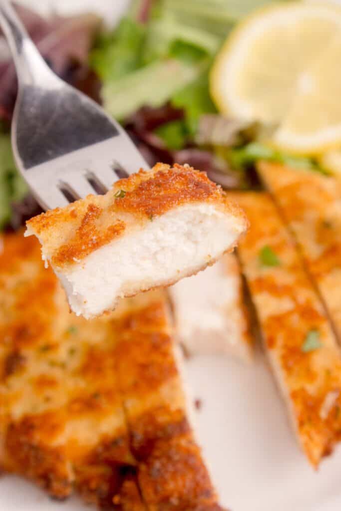 Dinner plate with breaded chicken cutlets. A fork is lifting up a bite.