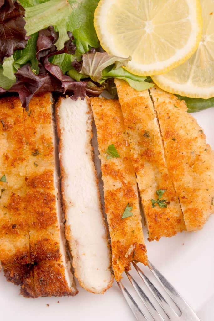 Sliced chicken cutlet. One slice is turned on it's side to show interior of cooked chicken.