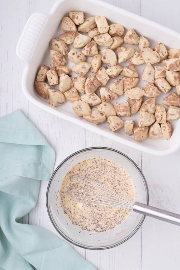 Baking dish lined with refrigerated cinnamon rolls quartered at the bottom of the pan. A glass bowl beside the baking dish has liquid ingredients and a whisk.