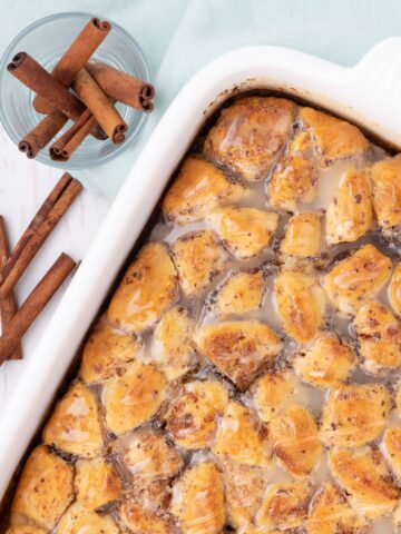 Casserole fresh out of the oven with a glaze drizzled over it. Cup of cinnamon sticks sits just above the baking dish.