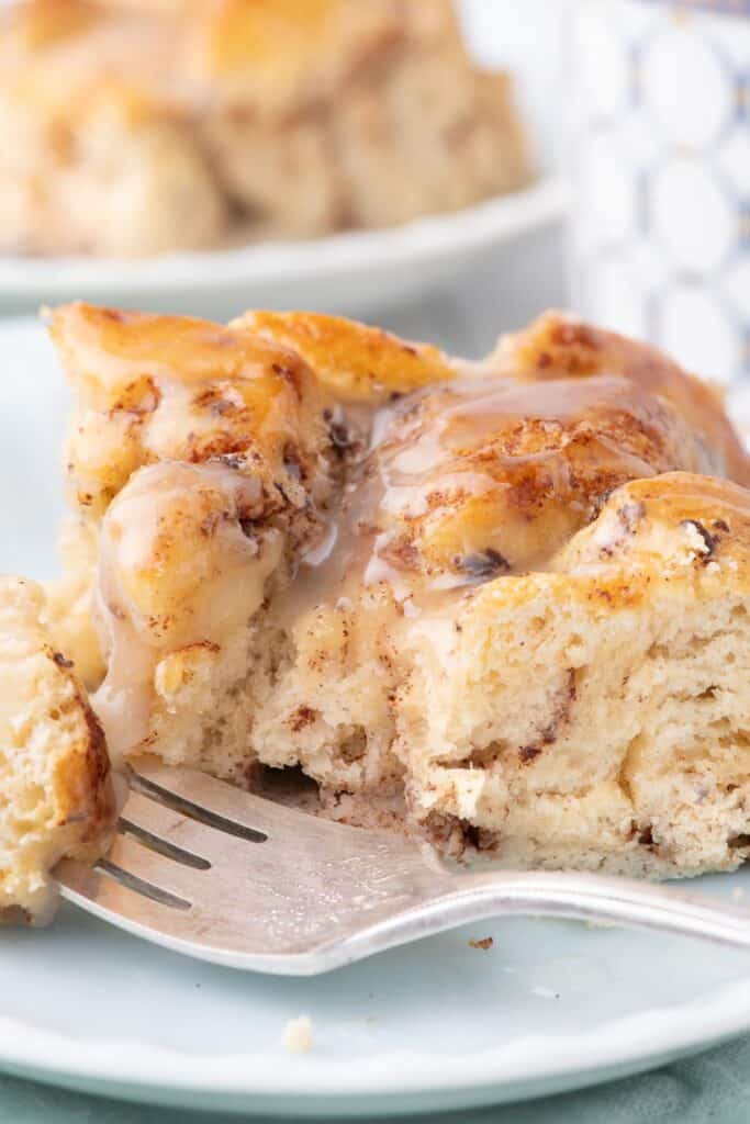 Cinnamon roll casserole on a white dinner plate with a bite on a fork.