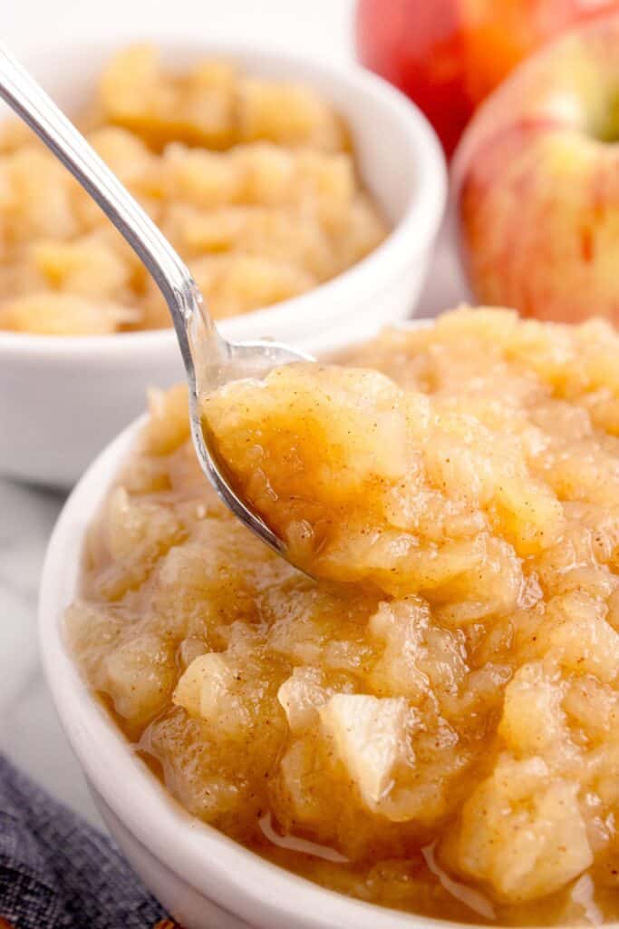 Close up view of applesauce in a bowl. A spoon is lifting a bite out of the bowl.