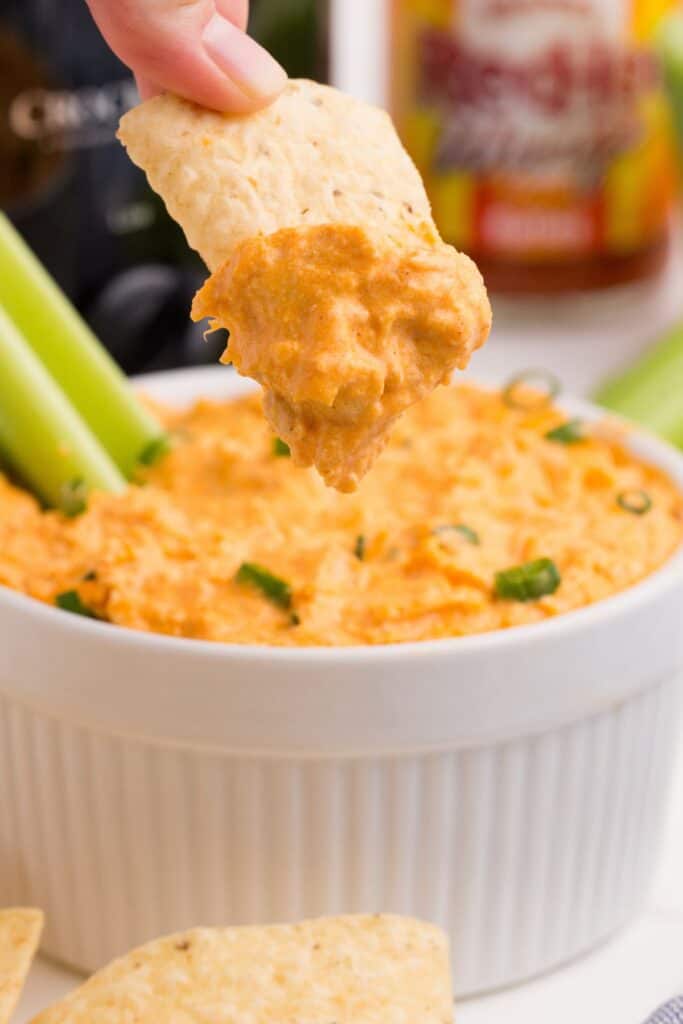 Buffalo chicken dip with a hand holding a dipped corn chip above the bowl.