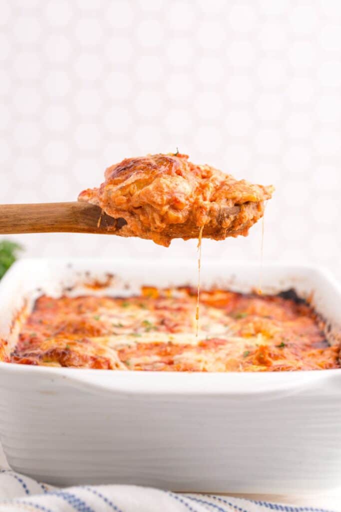 Side view of baking dish with lasagna. A wooden spoon is lifting a serving out of the dish.