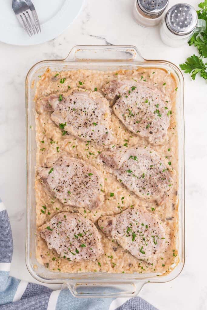 Baked casserole surrounded by a white dinner plate with forks, salt and pepper shakers, fresh parsley, and a tea towel.