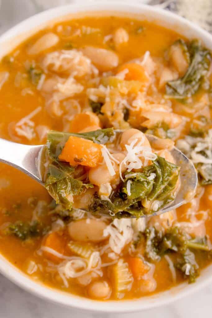 Bowl of white bean soup with a spoon lifting a bite above the bowl.