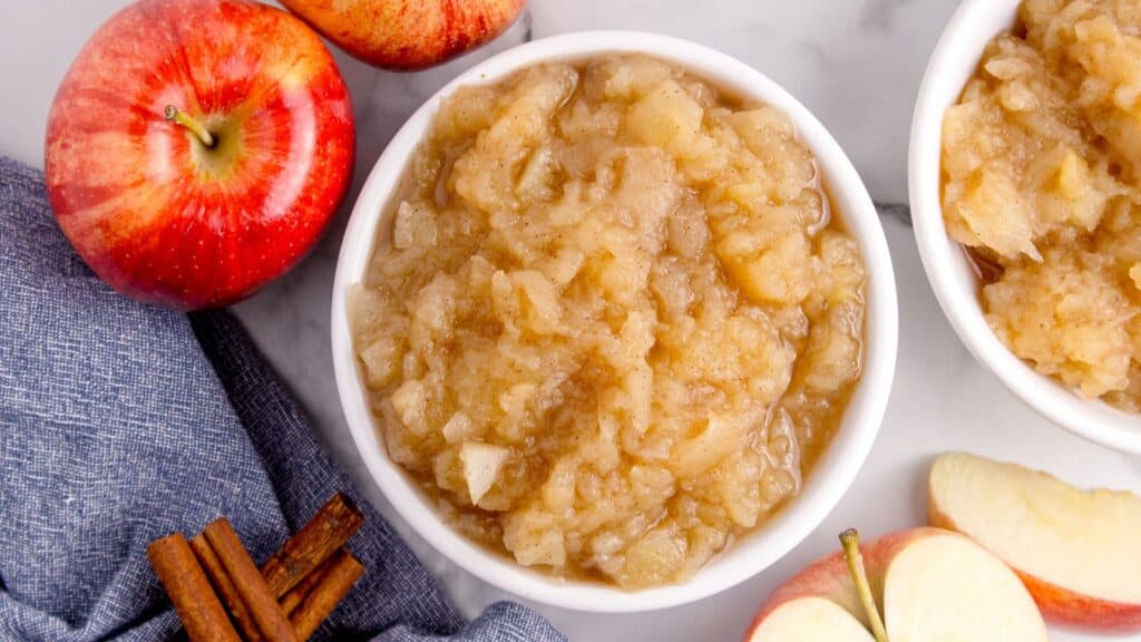 bowl of chunky applesauce overhead photo with apples and cinnamon sticks around the outside of the bowl.