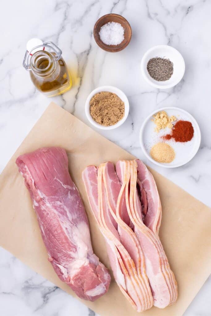 Ingredients for bacon wrapped pork tenderloin: pork tenderloin, bacon, brown sugar, salt, ground black pepper, smoked paprika, garlic powder, mustard powder, and olive oil.