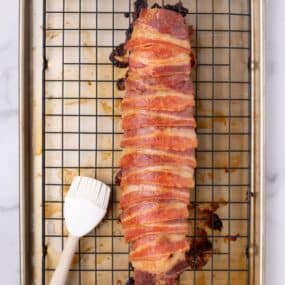 Tenderloin on a baking rack over a baking sheet. A silicone basting brush is next to it.