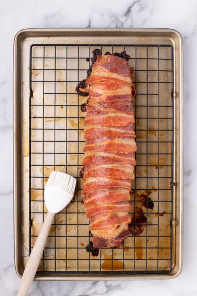 Tenderloin on a baking rack over a baking sheet. A silicone basting brush is next to it.