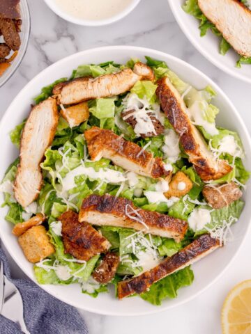 Prepared caesar salad with parmesan cheese and seasoned chicken on top.