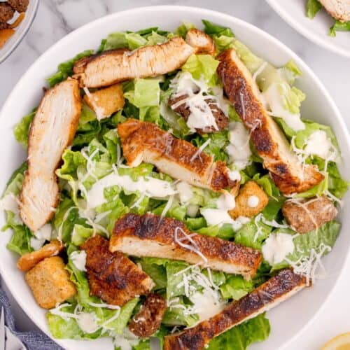 Prepared caesar salad with parmesan cheese and seasoned chicken on top.