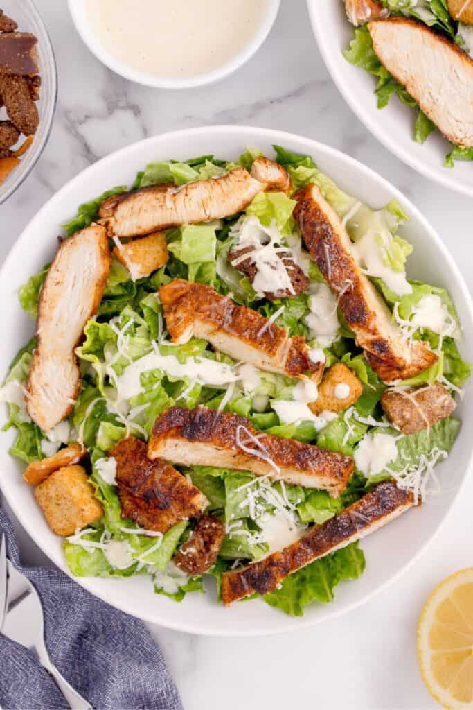 Prepared caesar salad with parmesan cheese and seasoned chicken on top.