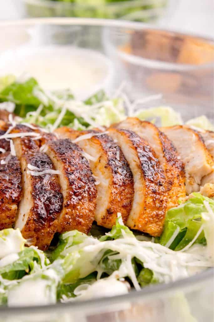 Close up of sliced chicken on a bed of lettuce, shredded parm, and caesar dressing.