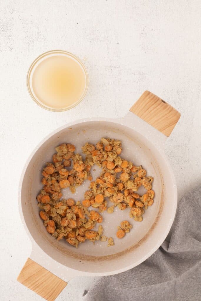 Butter, oil, carrots, and onion cooked together in a large pot. A small bowl of broth is in a glass bowl next to the pot.