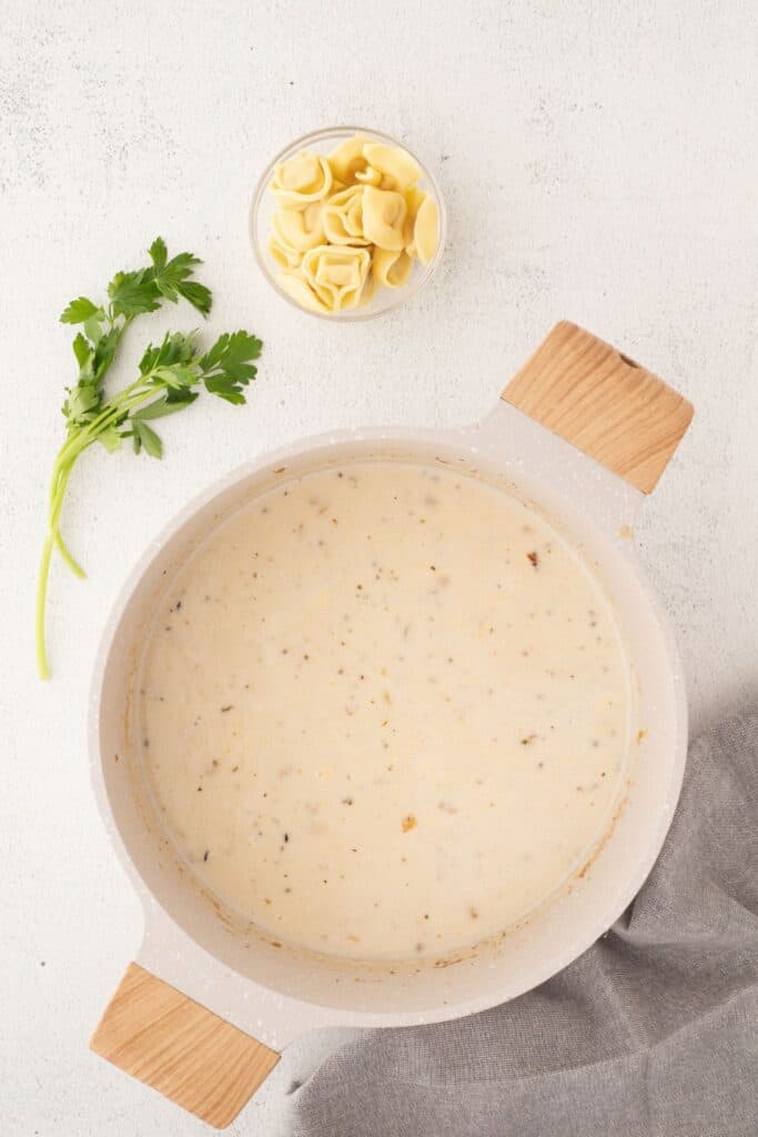 Soup base in a pot. Tortellini in a small glass bowl next to the pot.