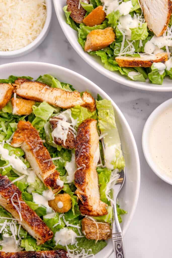 Two large salads shown side by side. Small bowls of dressing and parmesan surround the bowls of salad.