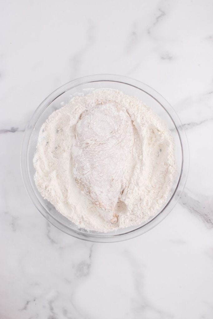 Raw chicken dredged in a bowl of flour.