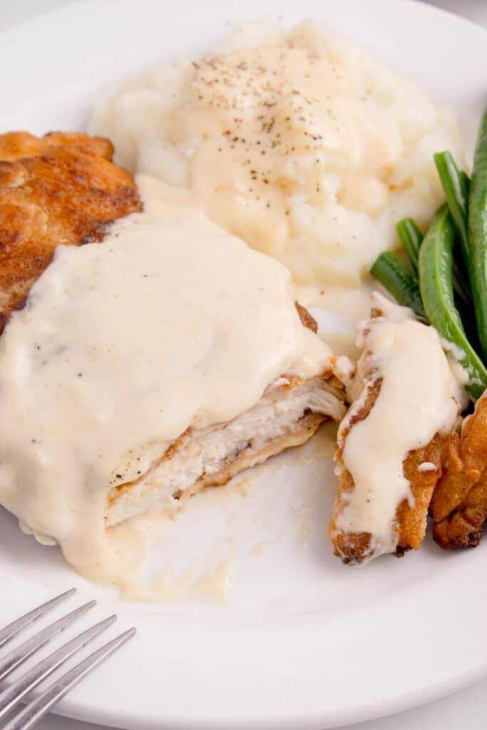 White dinner plate with green beans, mashed potatoes, and chicken fried chicken with gravy.