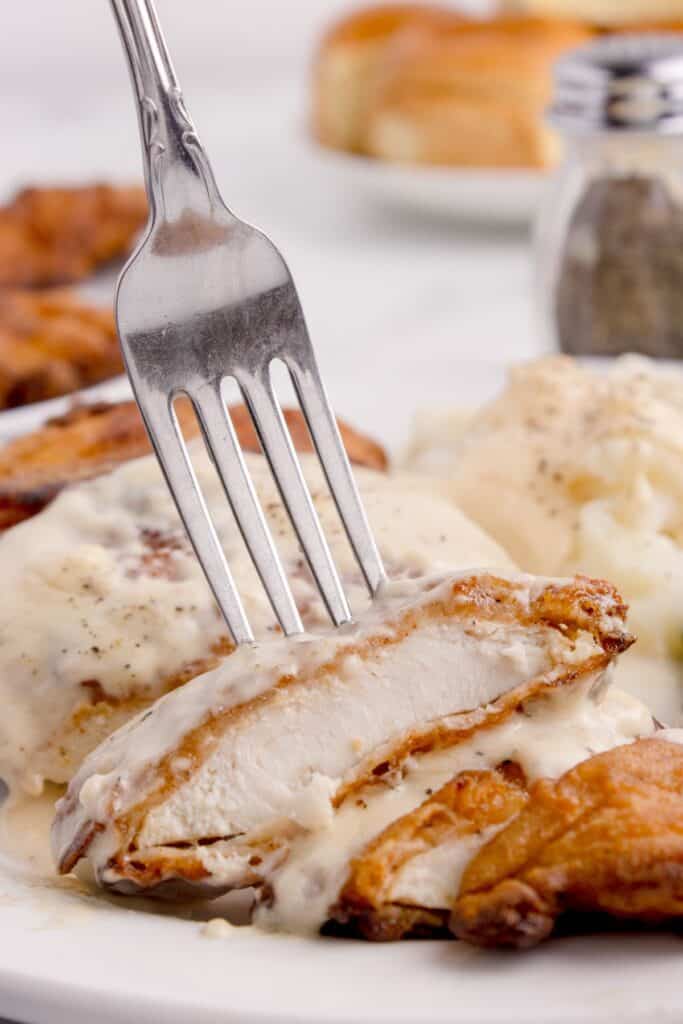 Close up of chicken fried chicken on a dinner plate. Fork is lifting a bite of chicken.