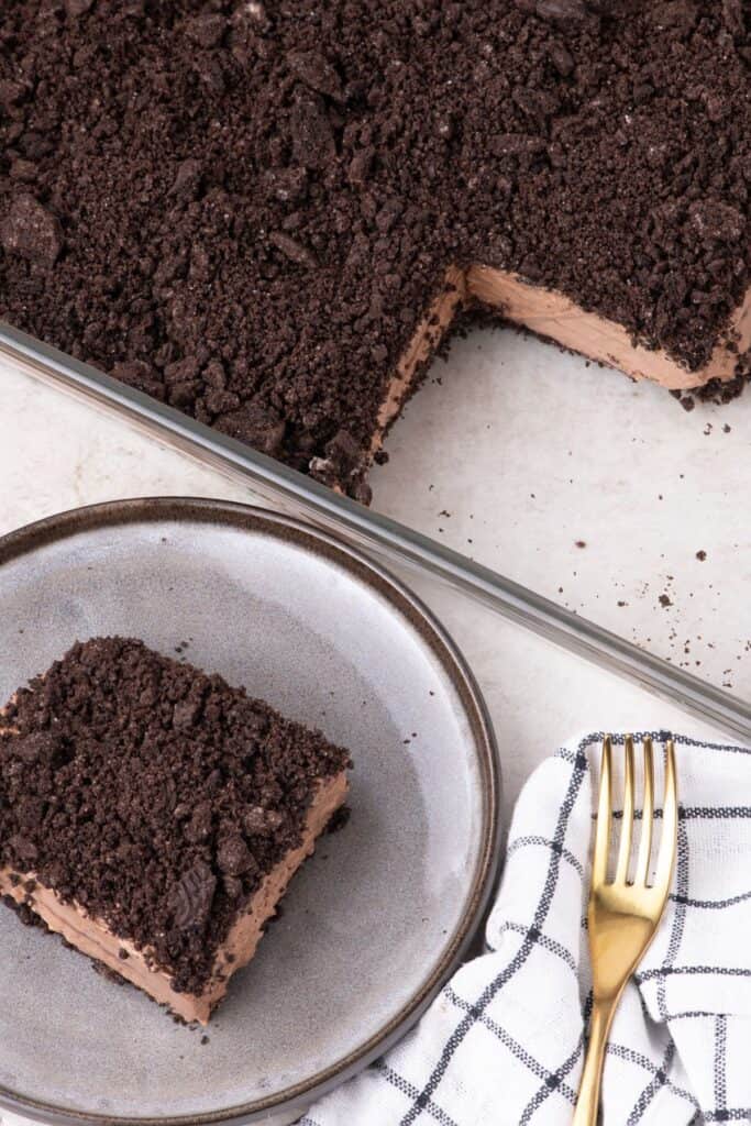 A slice of dirt cake on a plate next to a glass serving dish with the rest of the dirt cake.