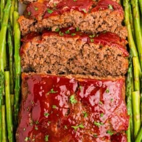 Completed and sliced meatloaf garnished with asparagus on both sides.