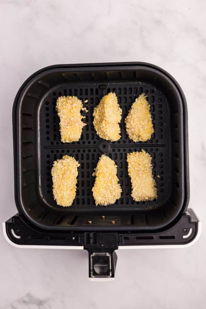 Breaded and uncooked fish sticks lined up in an air fryer basket.